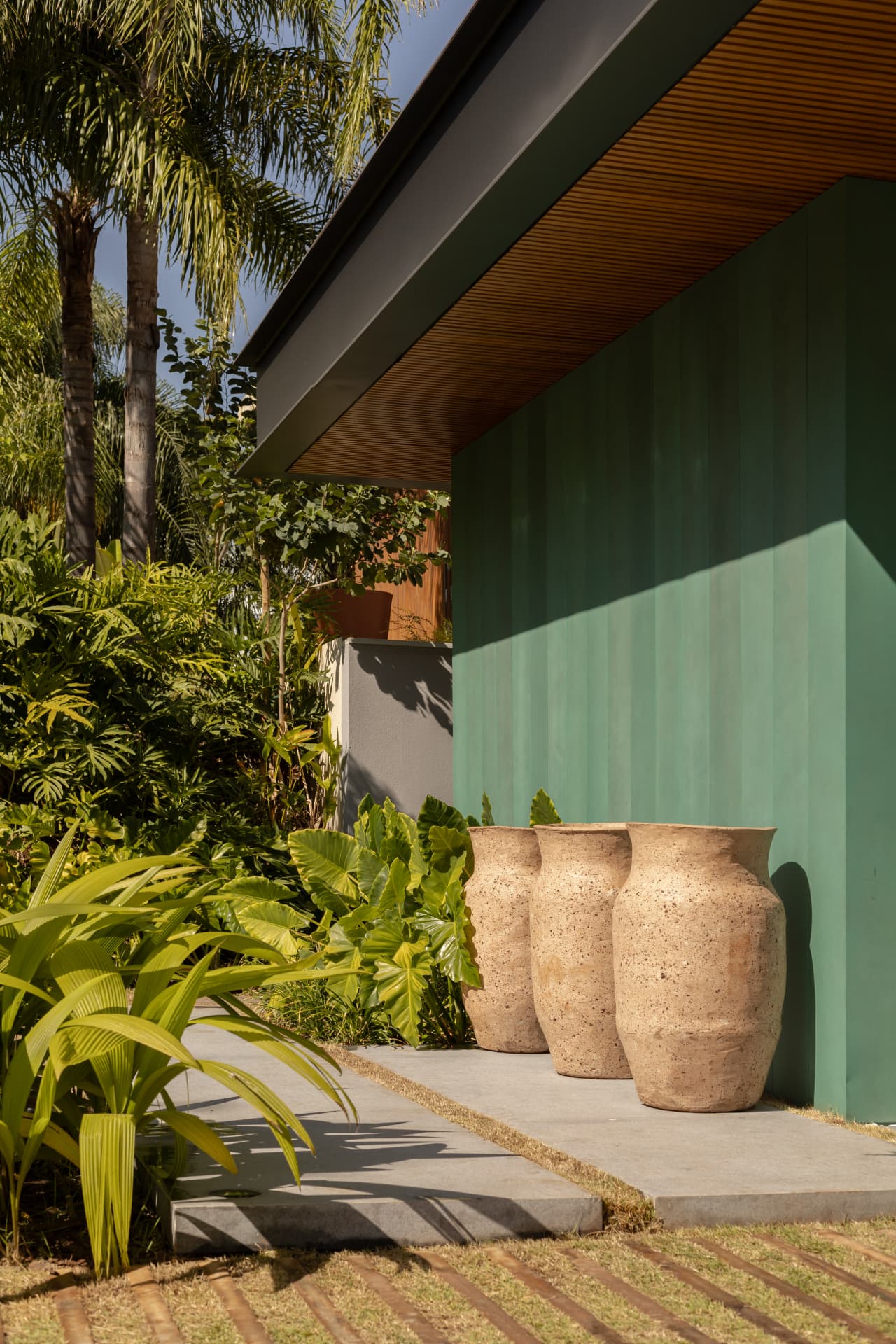 Vasos de pedra junto ao painel verde com palmeiras e sombra das folhagens