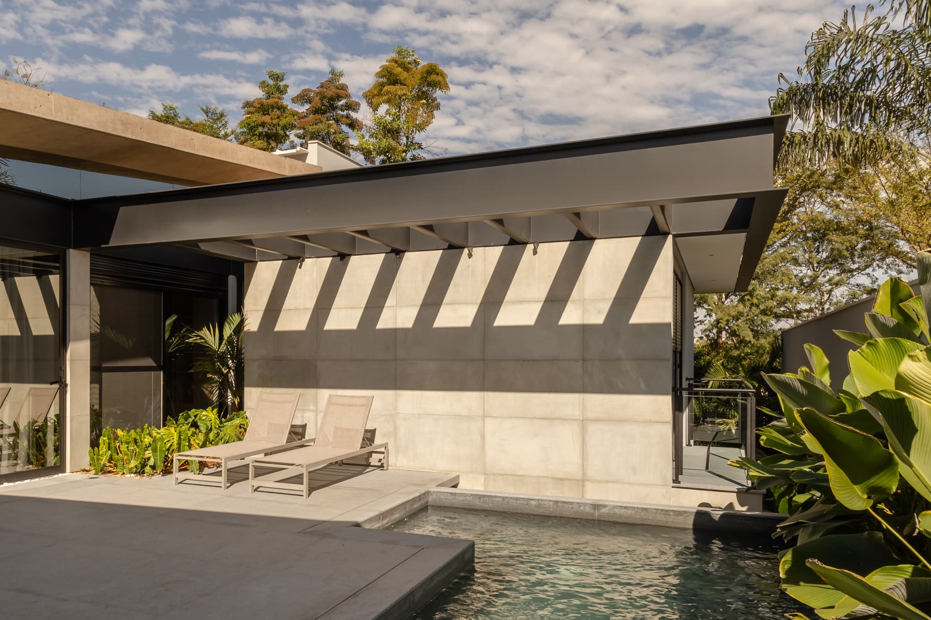 Piscina com deck, espreguiçadeiras e parede de concreto aparente