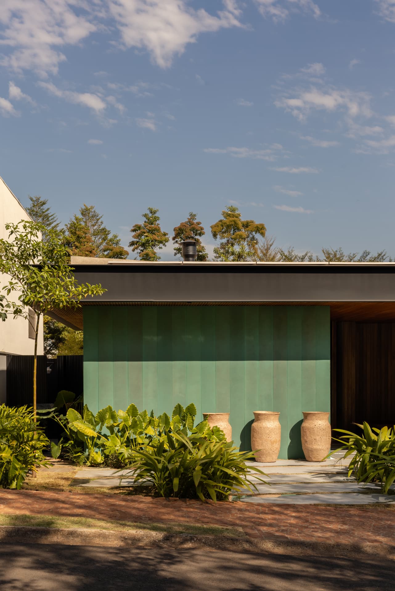 Fachada com painel verde, vasos de pedra e vegetação tropical